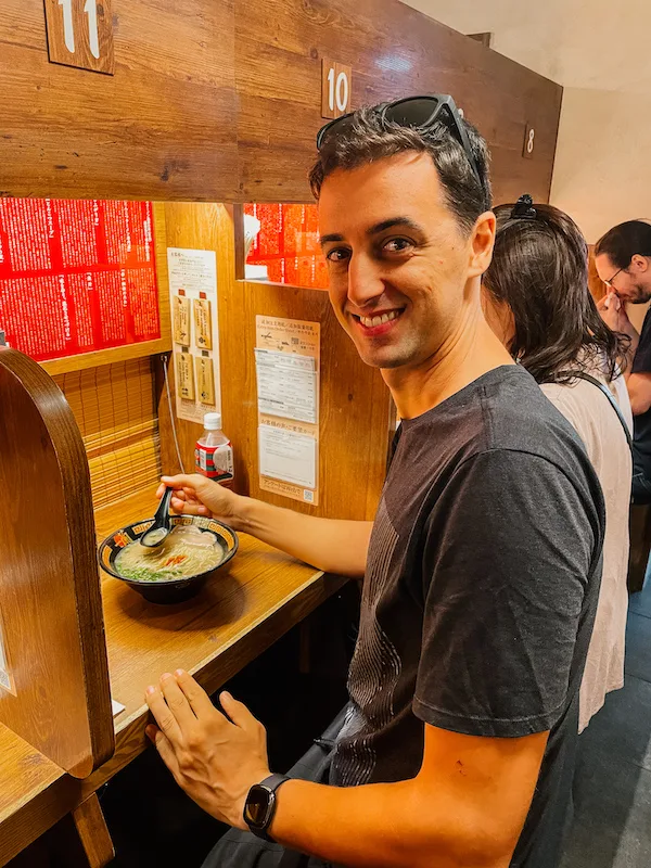 A man sitting in front of a small table with a bowl of ramen 