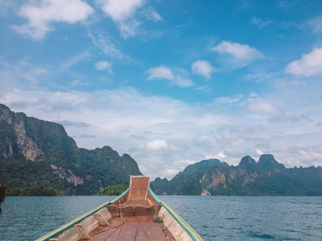 A longtail boat sailing on a late, and massive limestone cliffs covered in vegetation 