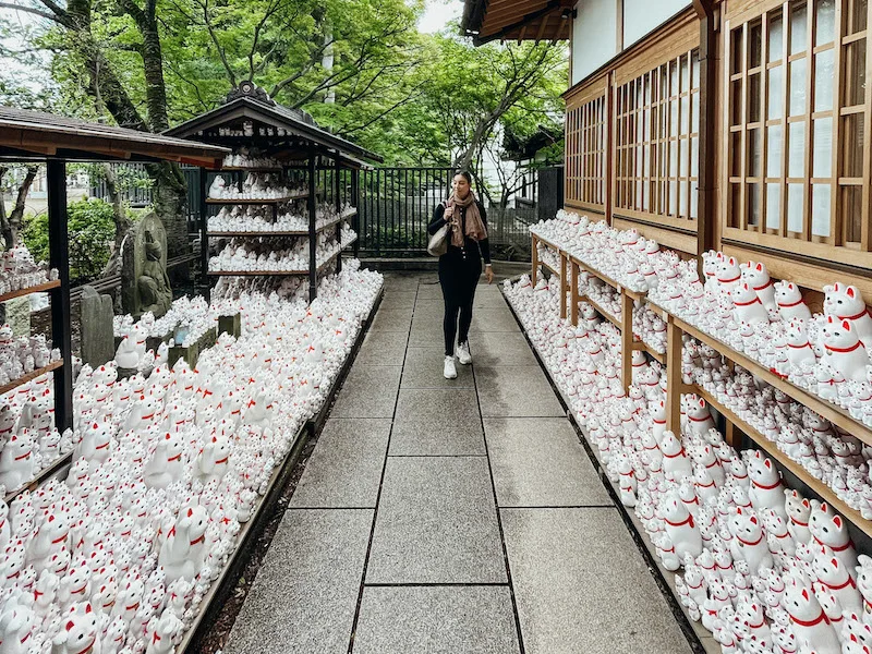 A woman walking around a temple, lined by thousands of Maneki Neko cat figurines