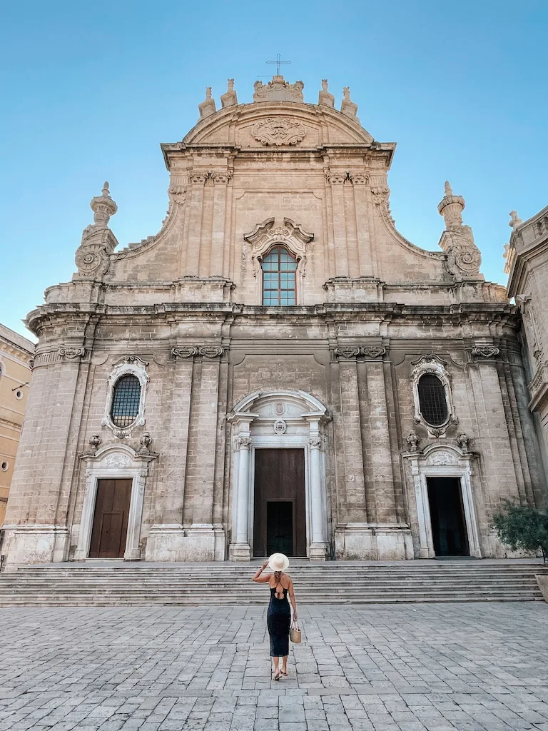 A woman in a black dress and a hat in front of a church 