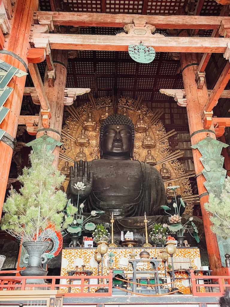 A shrine with a metal and golden buddha inside a red temple in Nara, Japan.