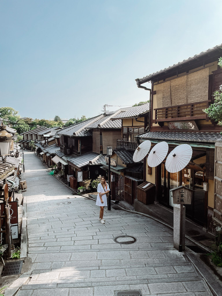 A woman in a white dress walking along a cobblestone alley lined by traditinoal Japanese houses