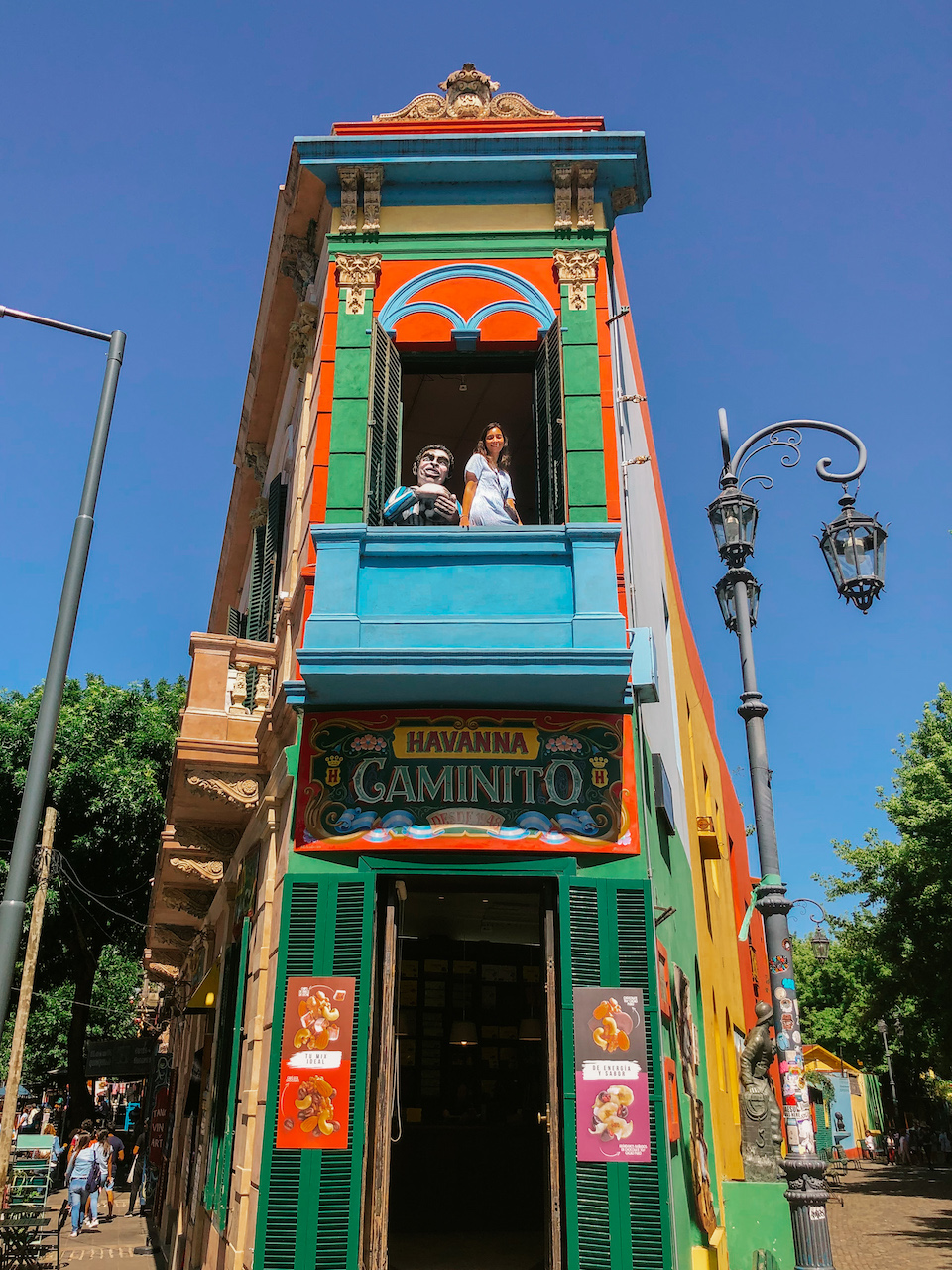 A colorful corner building and a woman standing by the open window on the second floor