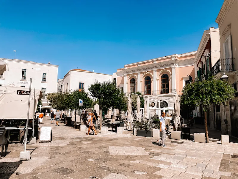 A small cobblestone square with buildings around it, and people walking through it 