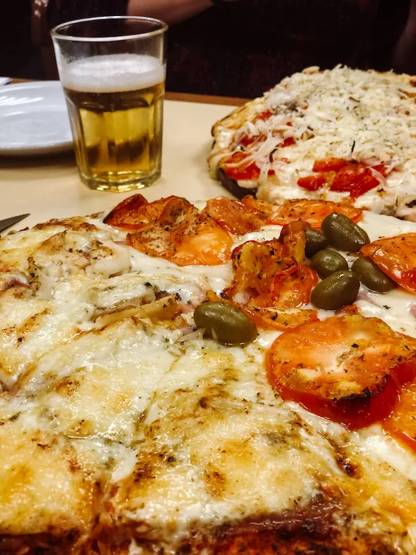 Close up image of a pizza, and a glass of beer behind it 