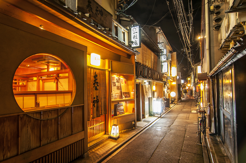 A narrow alley at night lined by restaurants with their lights on