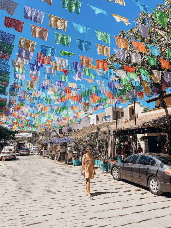 A woman walking along a street with colorful flags above it 