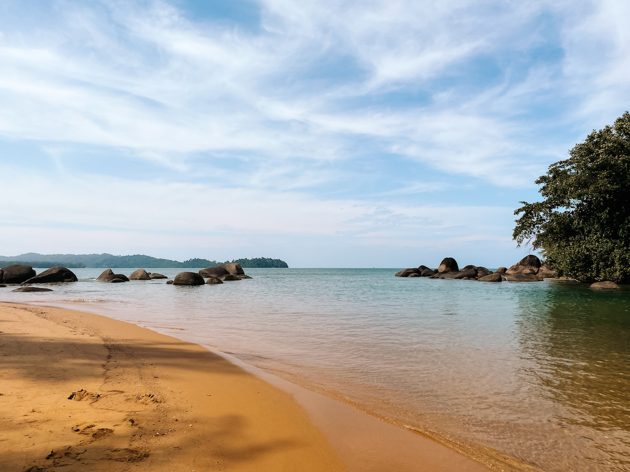 A tranquil beach with golden sand, rocks, and vegetation to the side