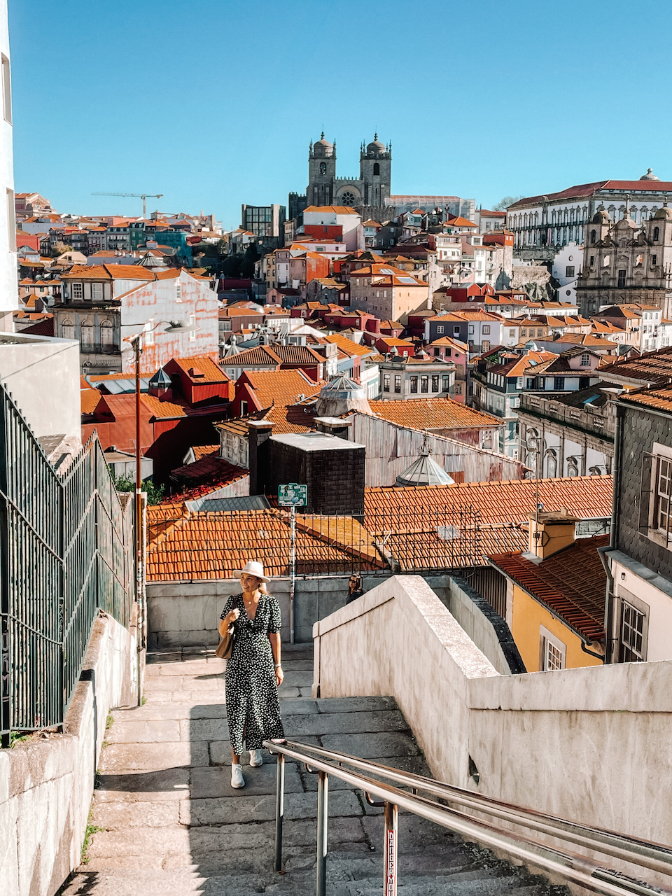 A woman at the bottom of a staircase, and the view of a city with terracotta roofs and a church in the distance 