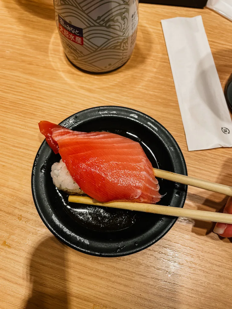 Two chopstick grabbing a piece of sushi from a small round black plate