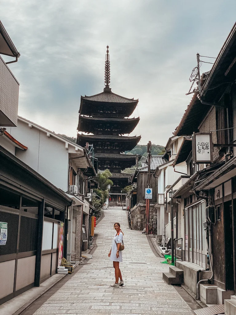 A woman with a white dress is smiling at the camera and standing in front of the Yasaka Pagoda in Kyoto.