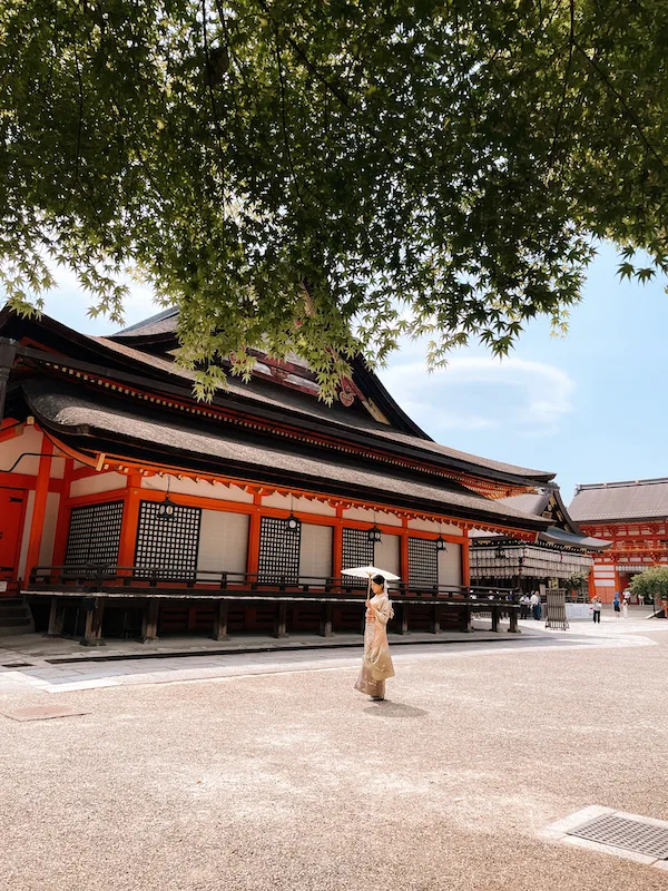 A Japanese temple, and a woman in a  kimono walking past it 