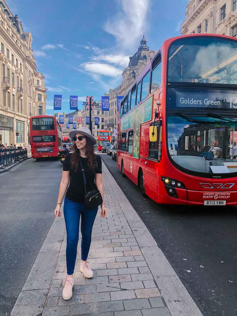 A woman walking between two roads with red double decker buses