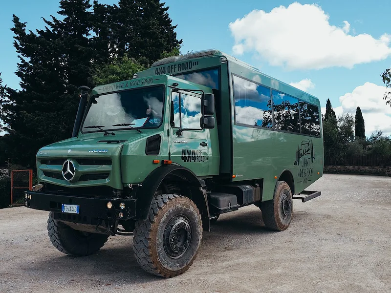 A rugged green 4x4 tour truck parked in a scenic countryside location in Tuscany.