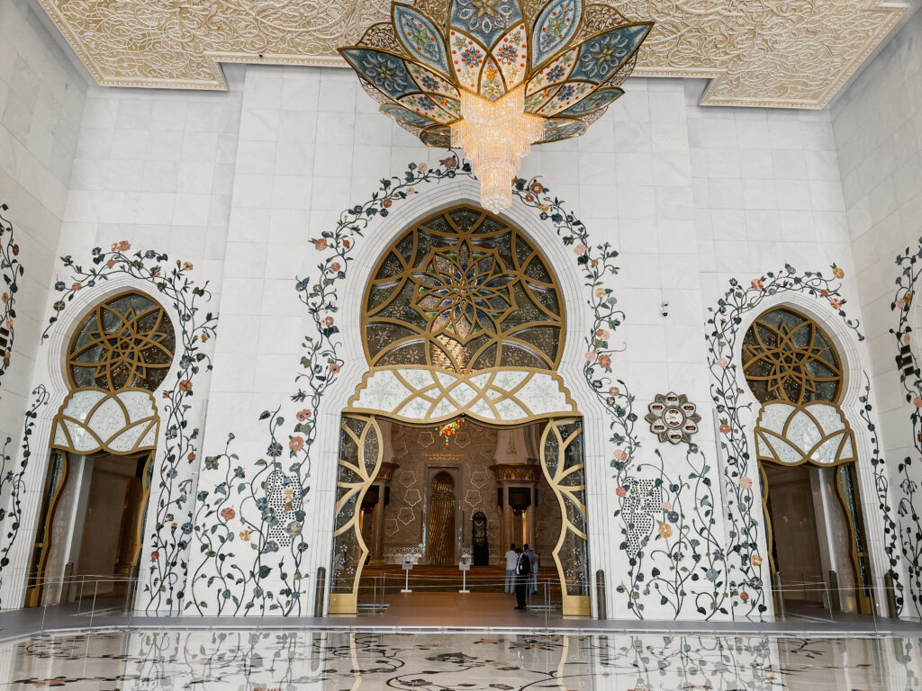 The breathtaking interior of Sheikh Zayed Grand Mosque, featuring intricate floral wall designs, golden chandeliers, and a high domed ceiling.