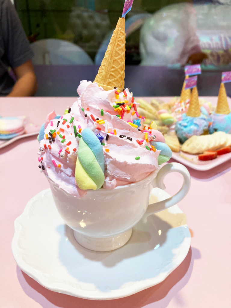 A white mug with pink whipped cream, sprinkles, and marshmallows on top