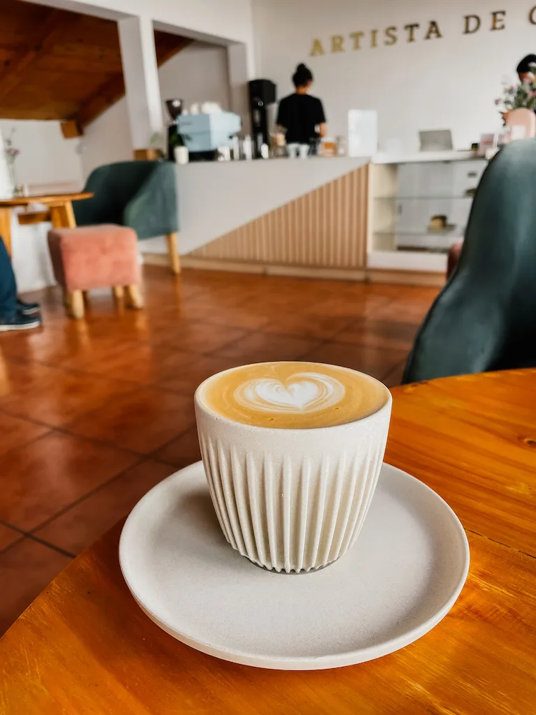 A mug with a latte on a table, and a coffee shop in the background