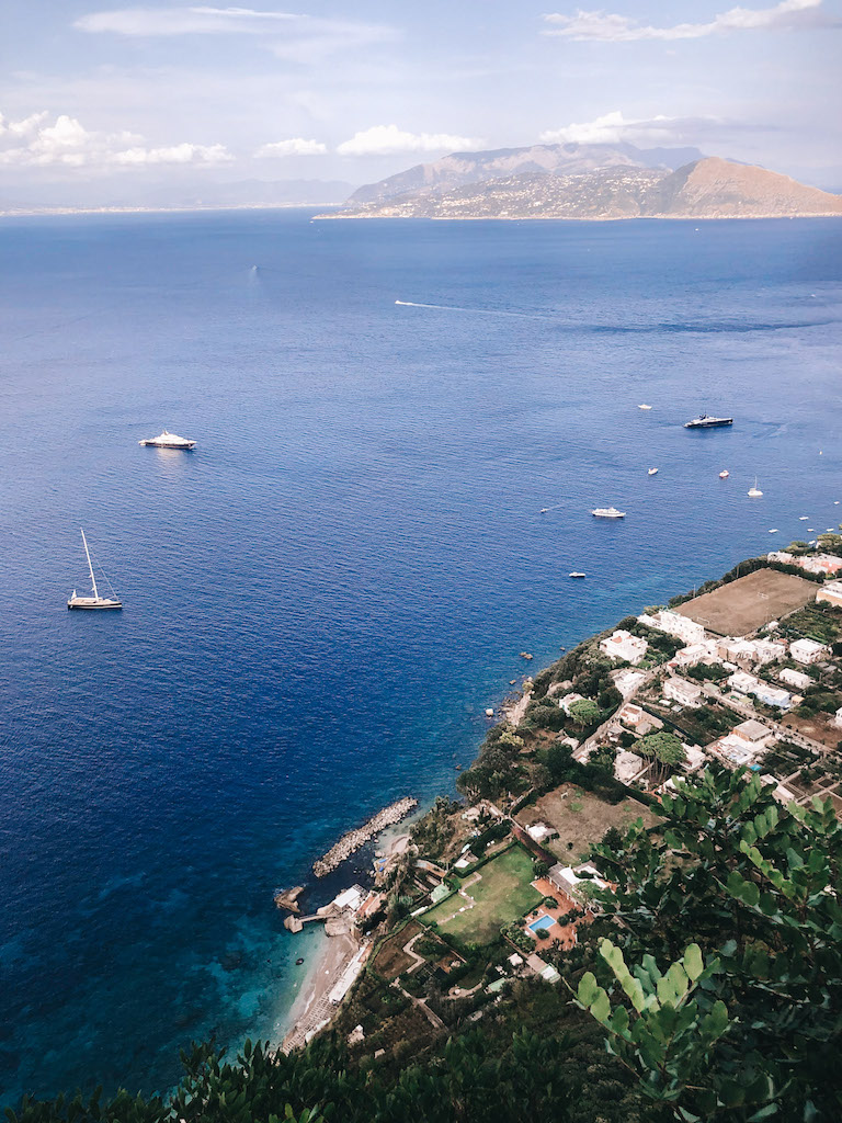 Aerial view of Capri’s coastline with boats and yachts on the water, overlooking the island’s rocky shores and green landscapes.