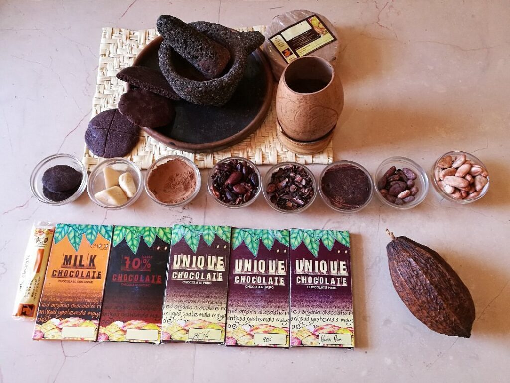 Chocolate bars on a table, with several bowls showing the various stages of cacao, form bean to powder, and a mortar and pestle