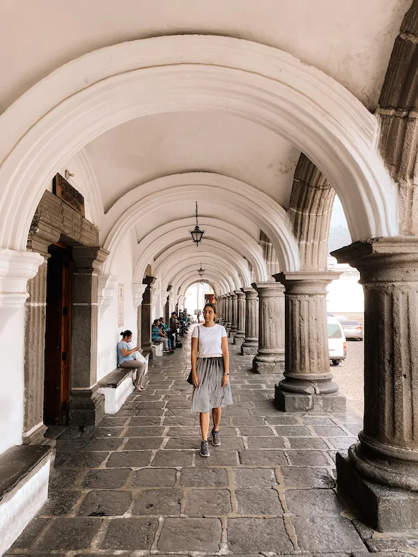 A woman walking along a portico with white arches and grey columns