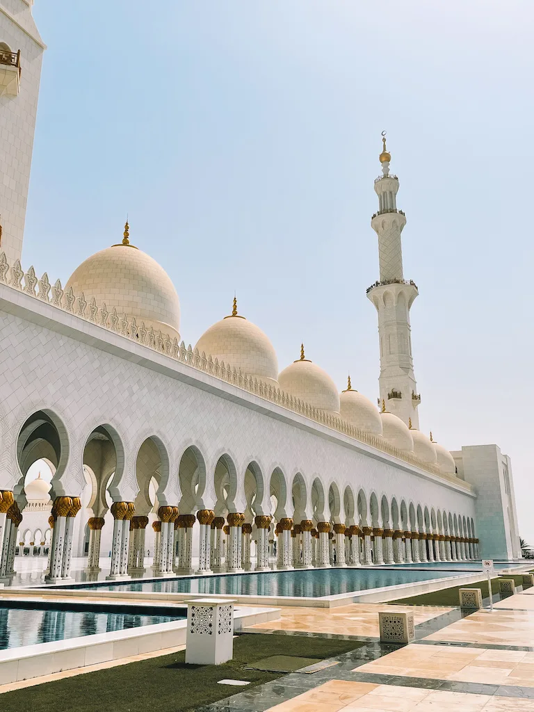 The grand exterior of Sheikh Zayed Grand Mosque, showcasing its iconic domes and towering minaret against a clear sky.