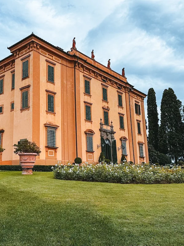 A grand historic villa with an orange facade, green shutters, and a manicured lawn.