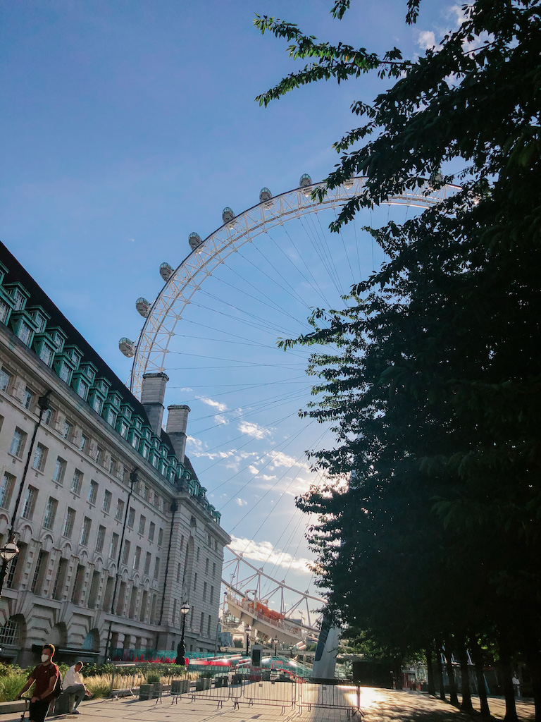 The London Eye Ferris Wheel, partially blocked by a tree on the right, and an elegant building on the left 