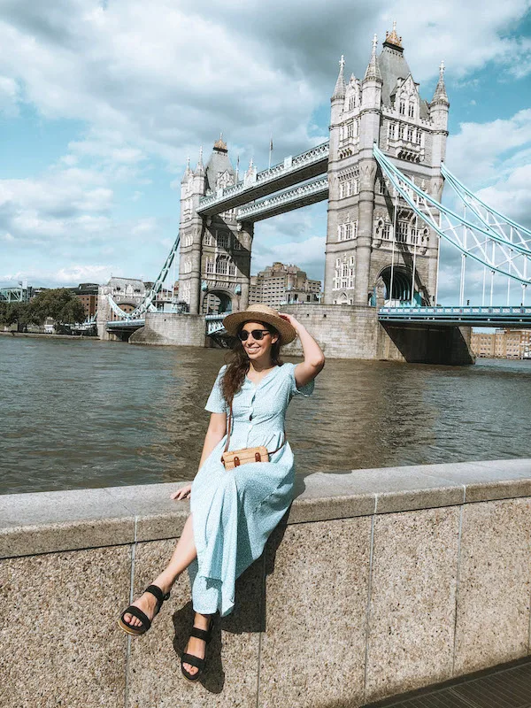 A woman in a blue dress sitting in front of the Tower Bridge in London