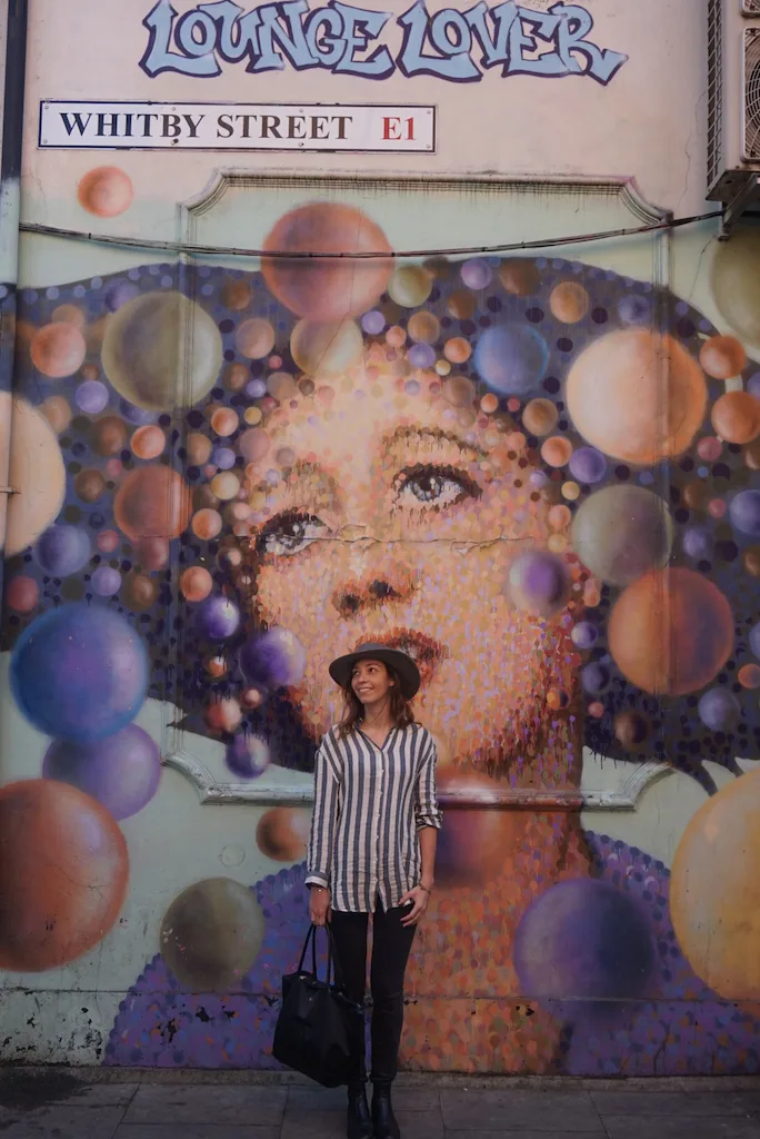 A woman standing in front of a mural with the image of a woman