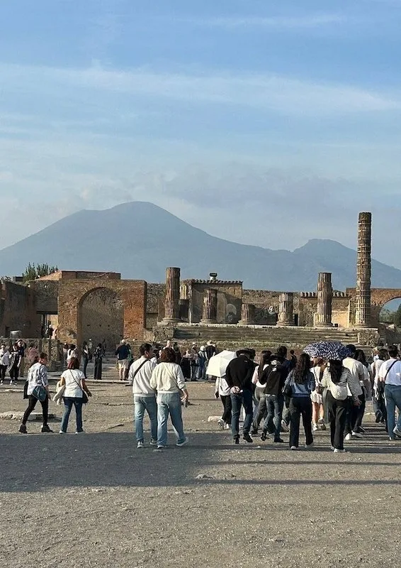 Tourists exploring the ancient ruins of Pompeii, with Mount Vesuvius looming in the background.