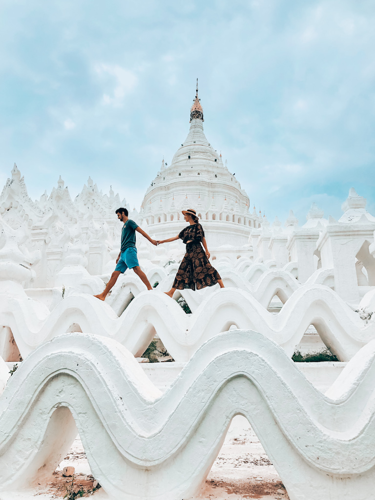 Couple exploring the stunning white architecture of Hsinbyume Pagoda in Myanmar, holding hands and walking along the wavy terraces. 