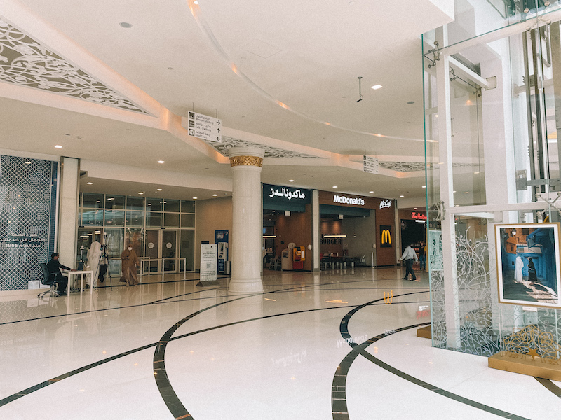 The entrance area near Sheikh Zayed Grand Mosque, featuring a McDonald's and other shops inside a modern, elegant space with white marble floors and gold detailing.