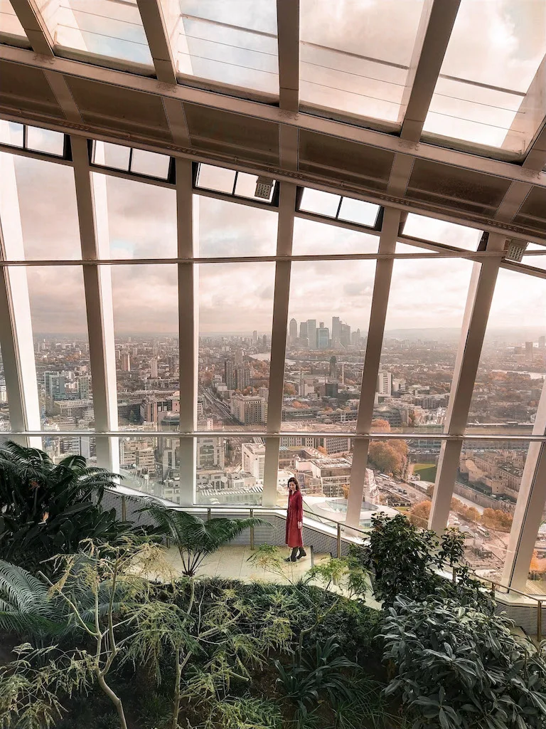 A woman in a long red dress standing in front of massive windows overlooking London