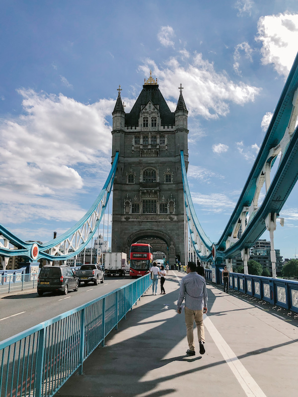 The Tower Bridge photographed from the middle of the bridge, with one of the towers in the center and people walking toward it 